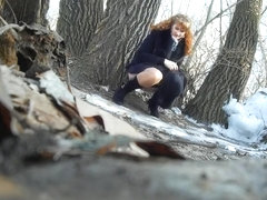 Ginger bridesmaid makes water behind a tree in the forest