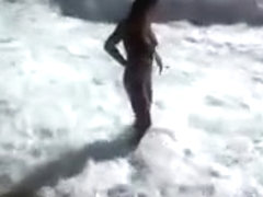 Busty brunette's lower part of a bikini drops as huge waves hit her